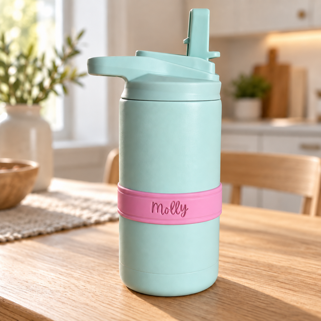 Seaglass-colored cup with a pink silicone bottle band personalized with the name Molly, sitting on a wooden table.